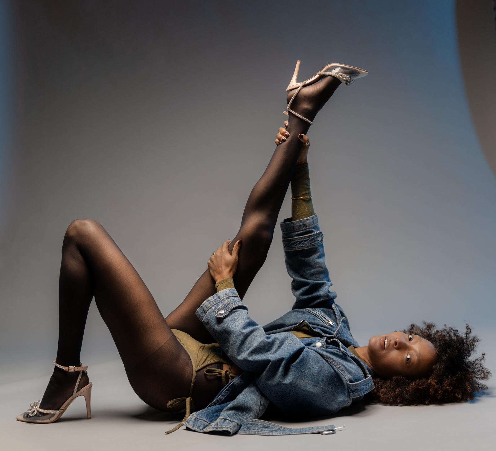 Editorial studio portrait, reclined with one leg lifted, denim and warm tones